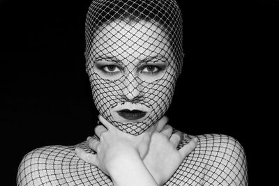 Portrait of young woman covered with net against black background