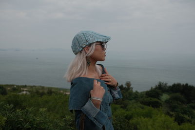 Side view of young woman standing against sky