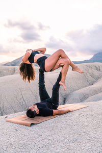 Woman balancing with namaste hands on legs of man while practicing acroyoga together in highlands