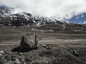 Scenic view of landscape and snowcapped mountains against cloudy sky