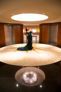 Woman standing by illuminated lamp on table