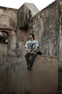 Full length of young man sitting outside building