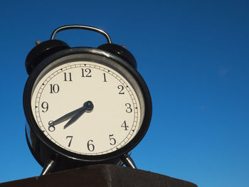 Low angle view of alarm clock against clear blue sky