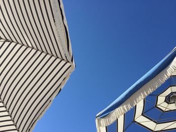 Low angle view of parasols against clear blue sky