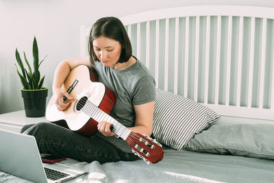 Young woman playing guitar while sitting on sofa at home
