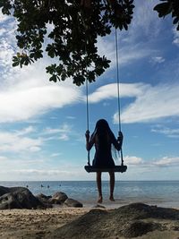 Low angle view of man swinging at beach against sky