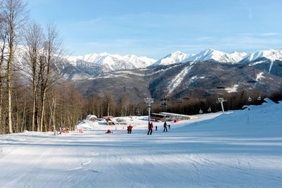 Gentle ski slope against the backdrop of a chairlift, snowy mountains and blue skies.