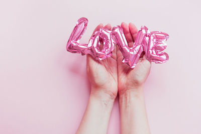 Close-up of hand holding pink flower over white background