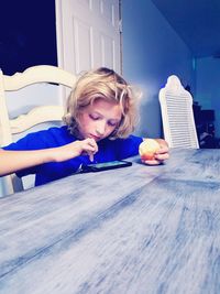 Boy holding apple while using smart phone on table at home