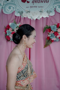 Woman looking away while standing against pink wall