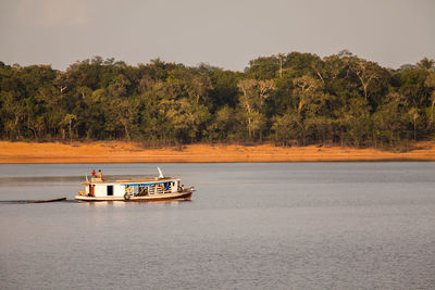 Boat sailing on river by trees against sky