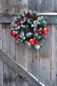 Green christmas wreath hanging on old vintage grey wooden door to cozy village house snowy winter.