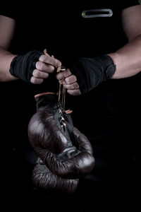 Midsection of man holding boxing gloves against black background