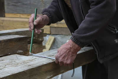 Midsection of carpenter measuring wood while working in carpentry workshop