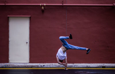 Full length of young man doing cartwheel by maroon building