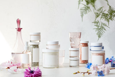 Close-up of white flowers in jar on table against wall