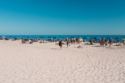 People at beach against clear blue sky