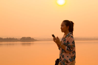 Young woman using mobile phone against sky during sunset