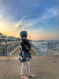 Rear view of woman by sea against sky during sunset