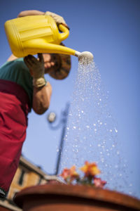 From below mature woman watering flowers on a sunny day
