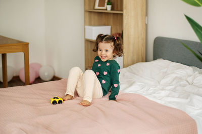 A charming little girl is playing with a car on the bed and fooling around