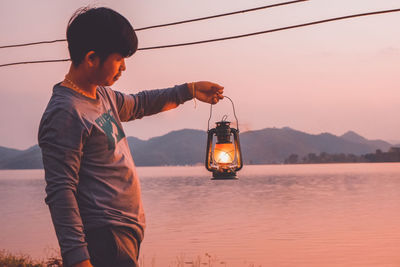 Man standing in lake against sky during sunset