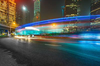 Illuminated light trails on road amidst buildings in city at night