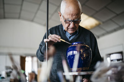 Senior man decorating ceramic vase in his spare time