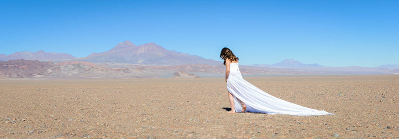 Woman in white dress walking on sand against clear sky