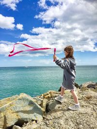 Rear view of boy standing by sea against sky