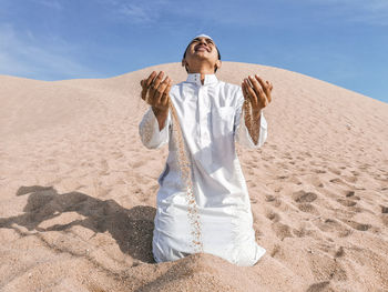 Man praying while kneeling on sand at desert