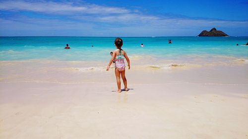 Full length rear view of girl standing on beach against sky