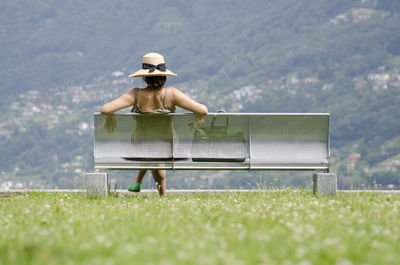 Rear view of woman sitting on bench against mountains at public park