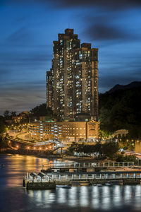 Illuminated buildings by sea against sky at night