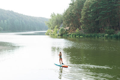 Woman surfing on lake against trees