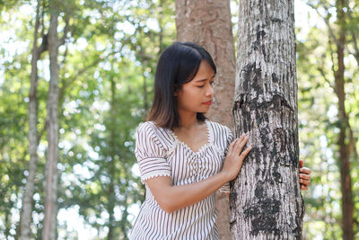 Mid adult woman standing against tree trunk