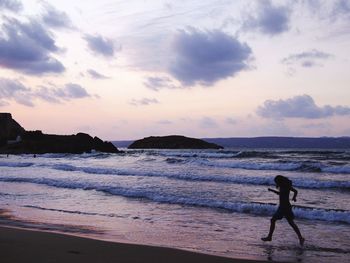 Silhouette woman standing on beach against sky during sunset