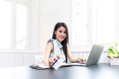Portrait of smiling young woman using phone while sitting on table