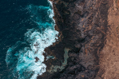 Beautiful drone shot of waves gently breaking on the shore with rocks, with blue color from above