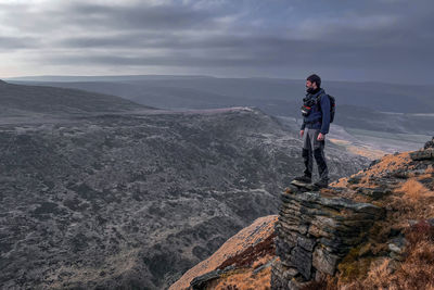 Lone hiker standing on cliff edge in the mountains overlooking the hills 