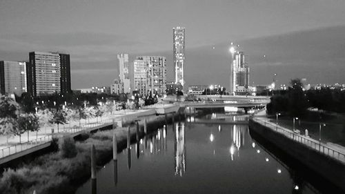 Illuminated city by river against sky