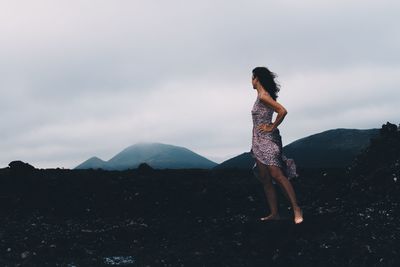 Side view of woman standing on mountain against sky