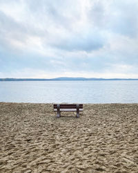 Empty bench on beach against sky