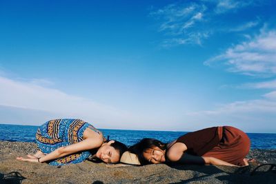 Portrait of friends bending on rocks at beach against sky