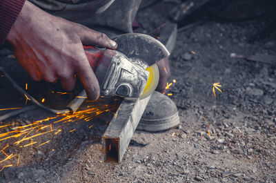 Low section of worker using power tool on metal at workshop