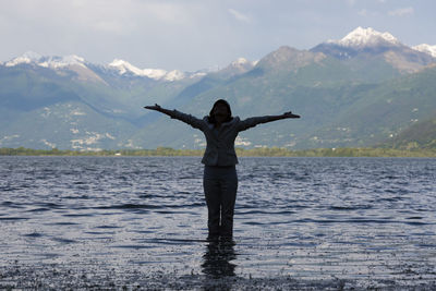 Woman standing with arms outstretched in lake maggiore against mountains