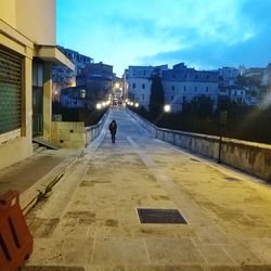 Man walking on illuminated road against sky in city