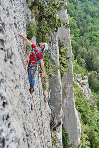 Side view of mountaineer in safety equipment climbing steep rock during summer vacation