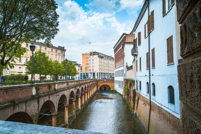 Bridge over river amidst buildings in city against sky