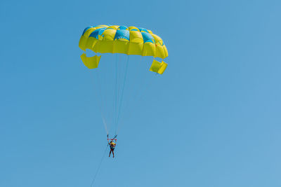 Low angle view of people paragliding against clear blue sky